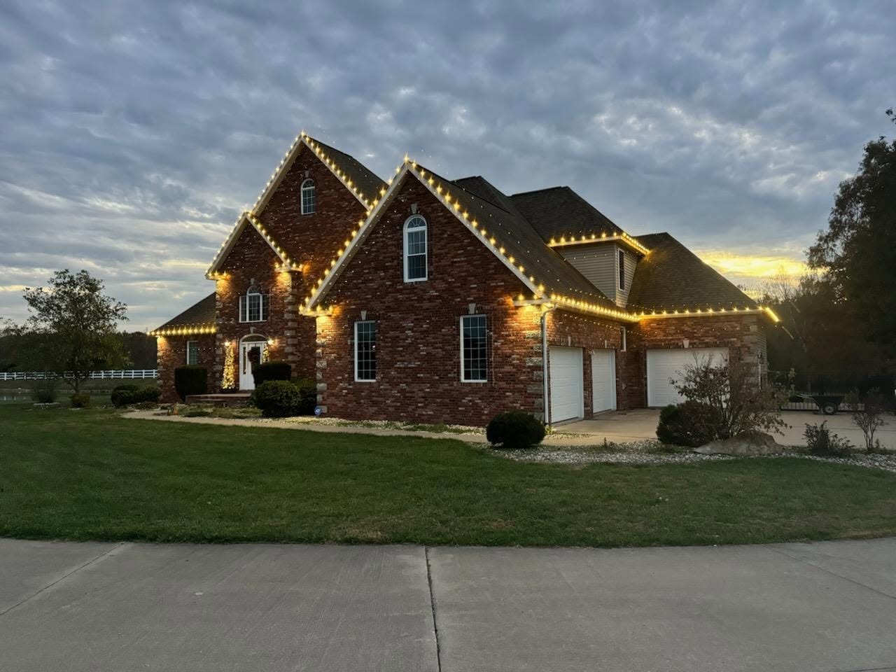 Brick estate with warm white roofline lights at twilight
